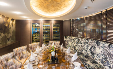 Elegant restaurant dining area aboard the AmaWaterways AmaLea with a round table set for twelve, featuring folded napkins, glassware, and floral decor; overhead lighting with a textured circular design.